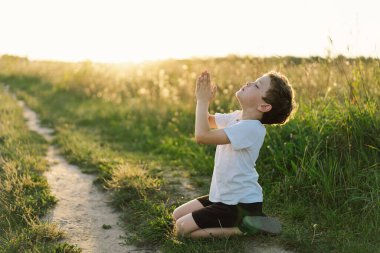 Oğlan gözlerini kapattı ve gün batımında bir tarlada dua etti. İnanç, maneviyat ve din için dua kavramına sarılmış eller..