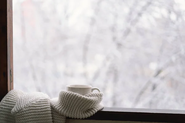 Cozy winter still life. Cup of hot tea with a warm sweater on a vintage wooden windowsill. Cozy home concept. Sweet home.