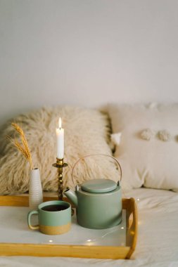 Bir fincan çay ve çaydanlık servis tepsisinde bir yatakta. Sabahları yatakta kahvaltı yapmak için. Evde çay içmenin, evde vakit geçirmenin konsepti. Sıcak bir sonbahar ya da kış konsepti.