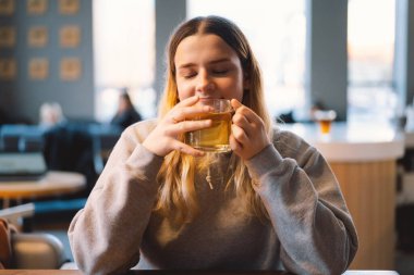 Kafede çay içen neşeli bir genç kızın portresi. Gülümseyen güzel kız kışın sıcak çay içer. Genç kız sıcak çay içiyor. Cafe City yaşam tarzı. Mutlu güzel kızın renkli portresi