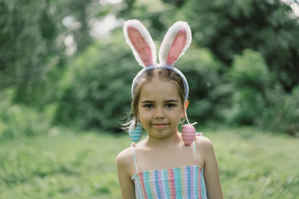 Easter egg hunt in spring garden. Funny girl with eggs basket and bunny ears on Easter egg hunt in garden. Children celebrating Easter. Happy easter card