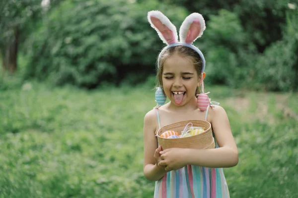 Easter egg hunt in spring garden. Funny girl with eggs basket and bunny ears on Easter egg hunt in garden. Children celebrating Easter. Happy easter card