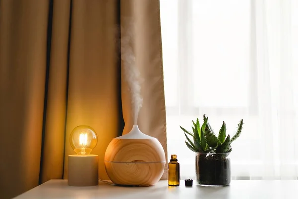Aromatherapy concept. Aroma oil diffuser on the table against the window. Air freshener. Ultrasonic aroma diffuser for home