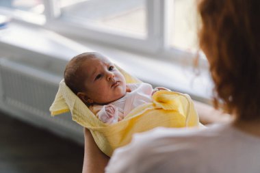 Portrait of happy mum holding infant child on hands. Loving mom carying of her newborn baby at home. Mother hugging her little 1 months old girl.