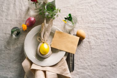 Happy Easter. Stylish easter eggs on a napkin with spring flowers on white wooden background. Table setting. The concept of a happy Easter holiday.