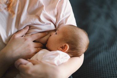 Newborn baby girl sucking milk from mothers breast. Portrait of mom and breastfeeding baby. Concept of healthy and natural baby breastfeeding nutrition.