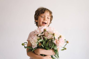Peonys buketli neşeli mutlu çocuk. Beyaz arka planda gülümseyen küçük çocuk. Anneler Günü. Aşk ve romantik konsept