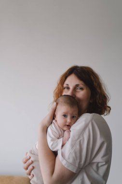 Bebek kucağında mutlu bir annenin portresi. Sevgi dolu anne, yeni doğmuş bebeğini evde taşıyor. Annesi 1 aylık küçük kızına sarılıyor..