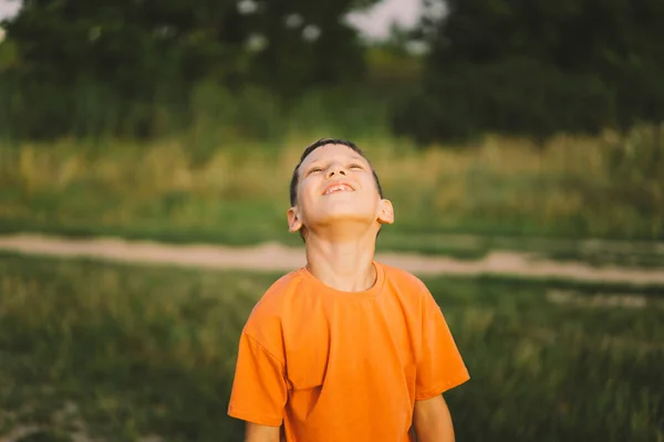 Portrait of a funny boy in a orange T-shirt and playing outdoors on the field at sunset. Happy child, lifestyle.