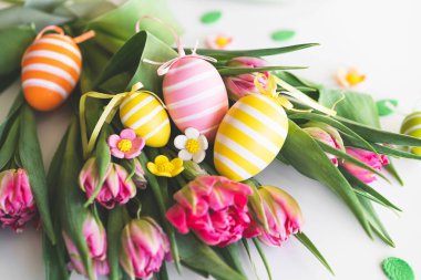 Happy Easter. Stylish dyed easter eggs with spring flowers on white background. Pink tulips with colorful eggs