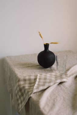 Modern dining table setting. A beautiful black vase with a linen napkin on the table. Only natural materials - earthenware, linen textiles, dried flowers.