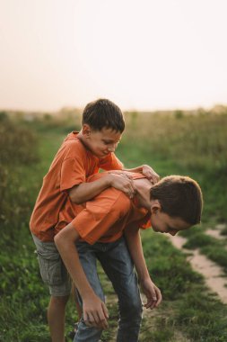 Turuncu tişörtlü komik çocuklar gün batımında sahada oynuyorlar. Mutlu çocuklar, yaşam tarzı..