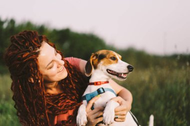 Güzel kadın parkta Jack Russell köpeğiyle oynuyor. Hayvanlar, arkadaşlık, insanlar ve aşk kavramı. Bir kadın çimlere uzanıyor ve Jack Russell Terrier ile oynuyor.