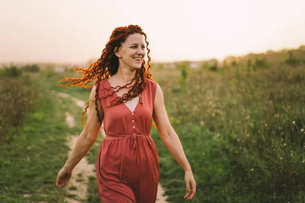 stock image Portraits of a charming red-haired woman with a cute face. Girl posing for the camera in the field at sunset.