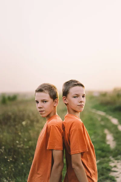 夕暮れ時に野外で遊ぶオレンジ色のTシャツの面白い双子の兄弟の男の子 幸せな子供たち ライフスタイル — ストック写真