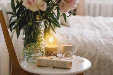 Still life details in home interior of living room. Open book with glasses, cup coffee and bouquet white pink peonies flowers. Read and rest. Cozy home clipart