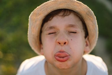 Gün batımında dışarıda oynayan beyaz tişörtlü ve şapkalı gülümseyen küçük bir çocuğun portresi. Mutlu çocuk, yaşam tarzı. Çocuklar için ürünler.