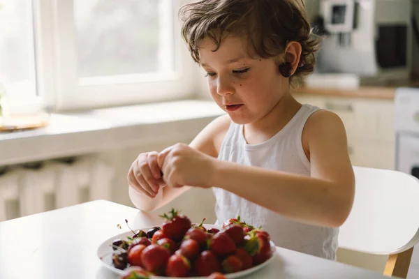 stock image Cute beautiful little boy eating fresh cherry and strawberry. Healthy food, childhood and development. Happy kid at home.