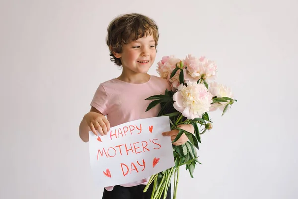 stock image Cheerful happy child with Peonys bouquet. Smiling little boy on white background. Mothers Day concept