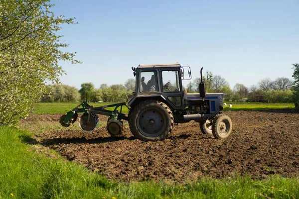 stock image The tractor drives across the field and cultivates the land. Agricultural vehicle works in countryside. Sowing is the process of planting seeds in the ground as part of the early spring time
