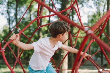 Oyun parkında ip örümceğin ağıyla oynayan mutlu çocuk. Çocuk sporları.