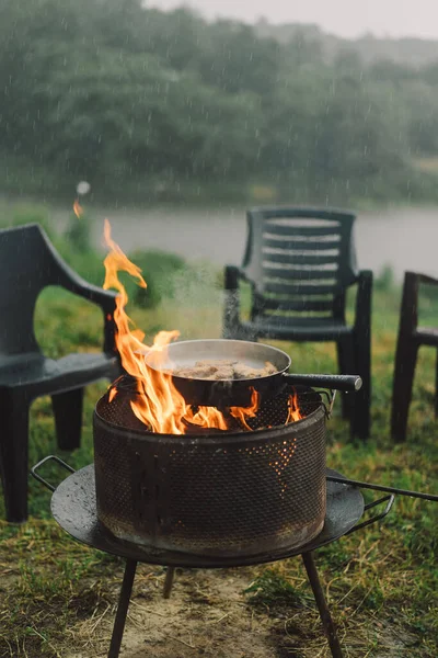 Cooking in the woods outdoors. Man cooking fish on fire in rainy weather, camping outdoors. Tourist on recreation outside. Campsite lifestyle