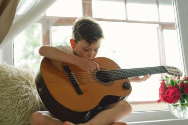 Tatlı çocuk pencerenin yanındaki pencere pervazında klasik gitar çalmayı öğreniyor. Rahat bir ev. Yaz tatili yaşam tarzı.