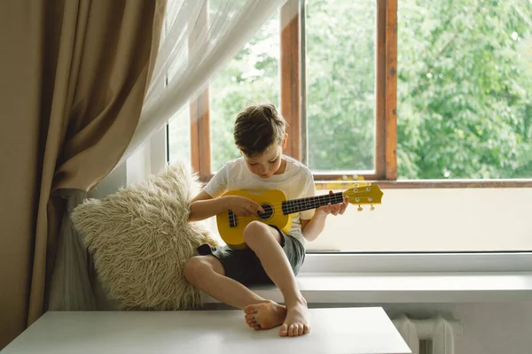Cute Boy Belajar Untuk Bermain Gitar Ukulele Kuning Jendela Dekat — Stok Foto