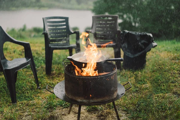 stock image Cooking in the woods outdoors. Man cooking fish on fire in rainy weather, camping outdoors. Tourist on recreation outside. Campsite lifestyle