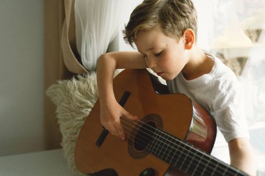 Tatlı çocuk pencerenin yanındaki pencere pervazında klasik gitar çalmayı öğreniyor. Rahat bir ev. Yaz tatili yaşam tarzı.