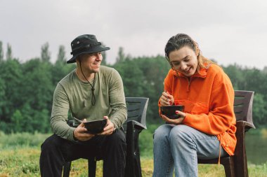 Bir erkek ve bir kadın ateşin yanında yemeğin tadını çıkarırlar. Ormanda şenlik ateşiyle yürüyüş kampı. Dışarıda tatil yapan bir turist. Kamp alanı yaşam tarzı