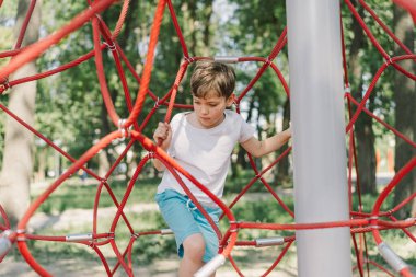 Oyun parkında ip örümceğin ağıyla oynayan mutlu çocuk. Çocuk sporları.