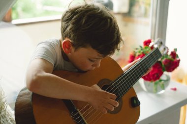 Tatlı çocuk pencerenin yanındaki pencere pervazında klasik gitar çalmayı öğreniyor. Rahat bir ev. Yaz tatili yaşam tarzı.