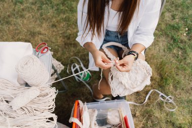 Çadırların yanında kadın makrome tekniği kullanarak çanta örüyor. Açık hava hobileri. Makrame dokuması.