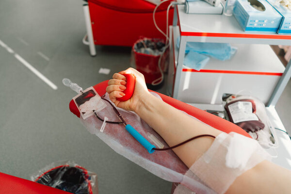 Young woman making blood donation in hospital. A woman donates blood while holding a red heart. Blood donation.