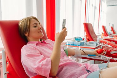 Telefonlu genç bir kadın hastanede kan bağışı yapıyor. Bir kadın kırmızı bir kalple kan bağışlıyor. Kan bağışı..