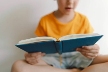 Turuncu tişört giyen sevimli bir çocuk yumuşak bir sedirin üzerinde oturmuş kitap okuyor. Uzayı kopyala Gerçek insanlar ve yaşam tarzı