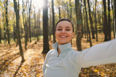 Güneşli bir sonbahar ormanında yürürken fotoğrafını çeken güzel bir kız. Macera, seyahat, tatil konsepti.