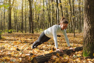 Güneşli bir sonbahar ormanında spor yapan güzel bir kız. Vücut pozitifliği, kadınlar için spor, uyum, sağlıklı yaşam tarzı, kendini sevme ve refah..