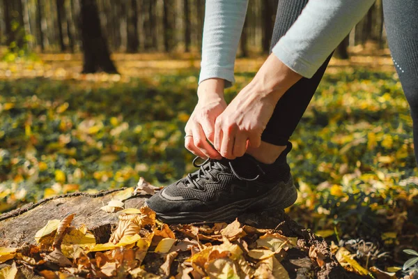 The girl ties her shoelaces. Beautiful girl doing fitness in nature on a sunny autumn forest. Body positive, sports for women, harmony, healthy lifestyle, self-love and wellness.