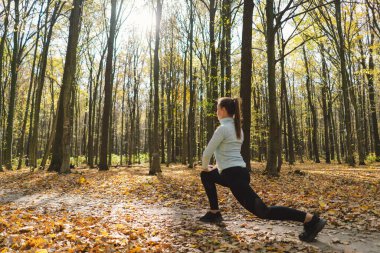 Güneşli bir sonbahar ormanında spor yapan güzel bir kız. Vücut pozitifliği, kadınlar için spor, uyum, sağlıklı yaşam tarzı, kendini sevme ve refah..