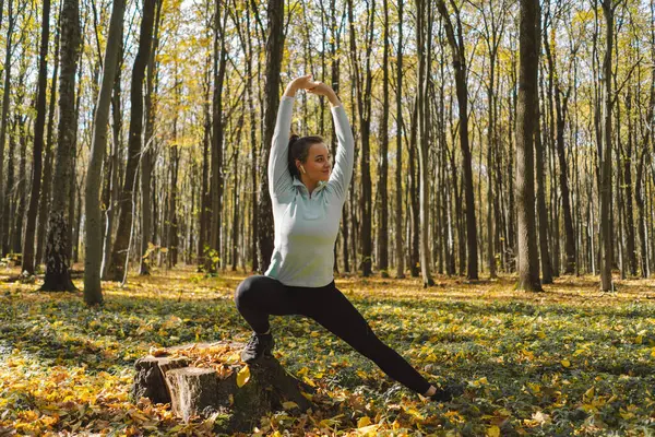 Güneşli bir sonbahar ormanında spor yapan güzel bir kız. Vücut pozitifliği, kadınlar için spor, uyum, sağlıklı yaşam tarzı, kendini sevme ve refah..