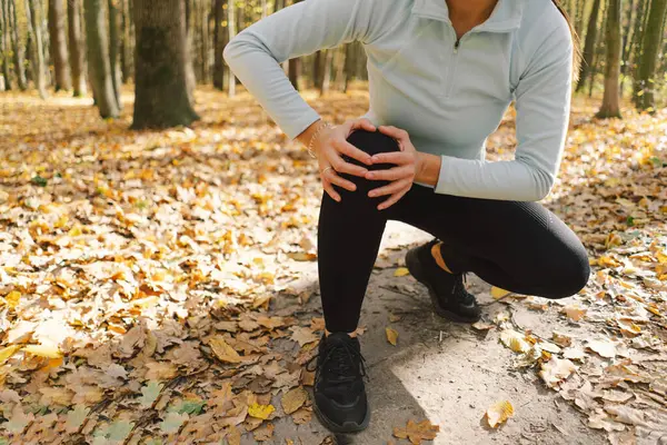 少女は痛み 秋の森での屋外トレーニング中に膝のスパムスプラインに苦しんでいます ロイヤリティフリーのストック画像