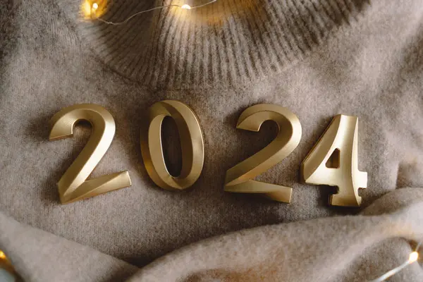 Holiday background Happy New Year 2024. Numbers of year 2024 with sweater and Christmas decorations together with lights bokeh on a gray background. Good New Year spirit. Ready postcard