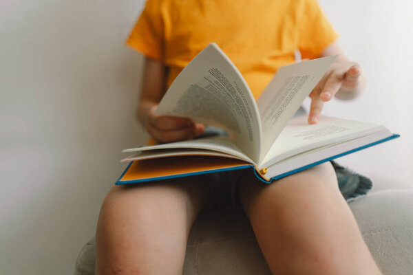 Симпатичный мальчик в оранжевой футболке сидит на мягкой оттоманке и читает книгу. Принято. Реальные люди и образ жизни