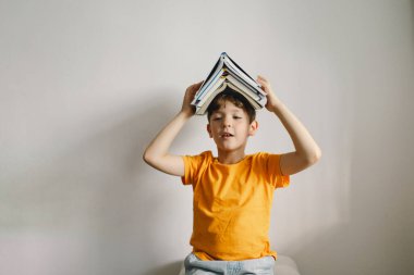 Turuncu tişört giyen sevimli bir çocuk yumuşak bir sedirin üzerinde oturmuş kitap okuyor. Uzayı kopyala Gerçek insanlar ve yaşam tarzı