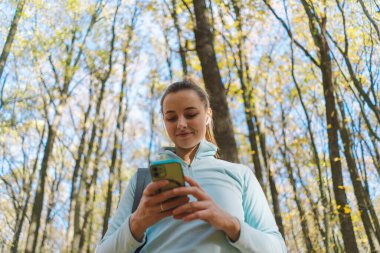 Güzel bir kız telefonu spor ya da yoga için kullanır. Vücut pozitifliği, kadınlar için spor, uyum, sağlıklı yaşam tarzı, kendini sevme ve refah..