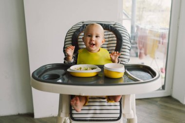 Sağlam beslenmiş küçük bir çocuk. Küçük kız parmak yemeği yiyor ve sebze tabağını karıştırıyor. Bebek sütten kesme BLW kendini besleme.