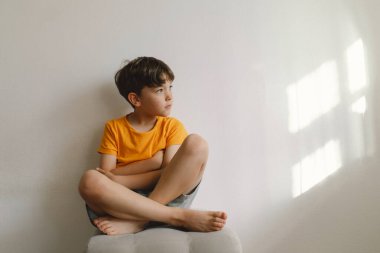 Bakımevinde yalınayak oturan tatlı çocuk. Güzel ışık. Esmer çocuk 7 yaşında, sıradan kıyafetler giyiyor. Rahat bir ev ve yaşam tarzı. Kapalı.