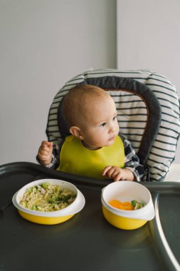 Sağlam beslenmiş küçük bir çocuk. Küçük kız parmak yemeği yiyor ve sebze tabağını karıştırıyor. Bebek sütten kesme BLW kendini besleme.